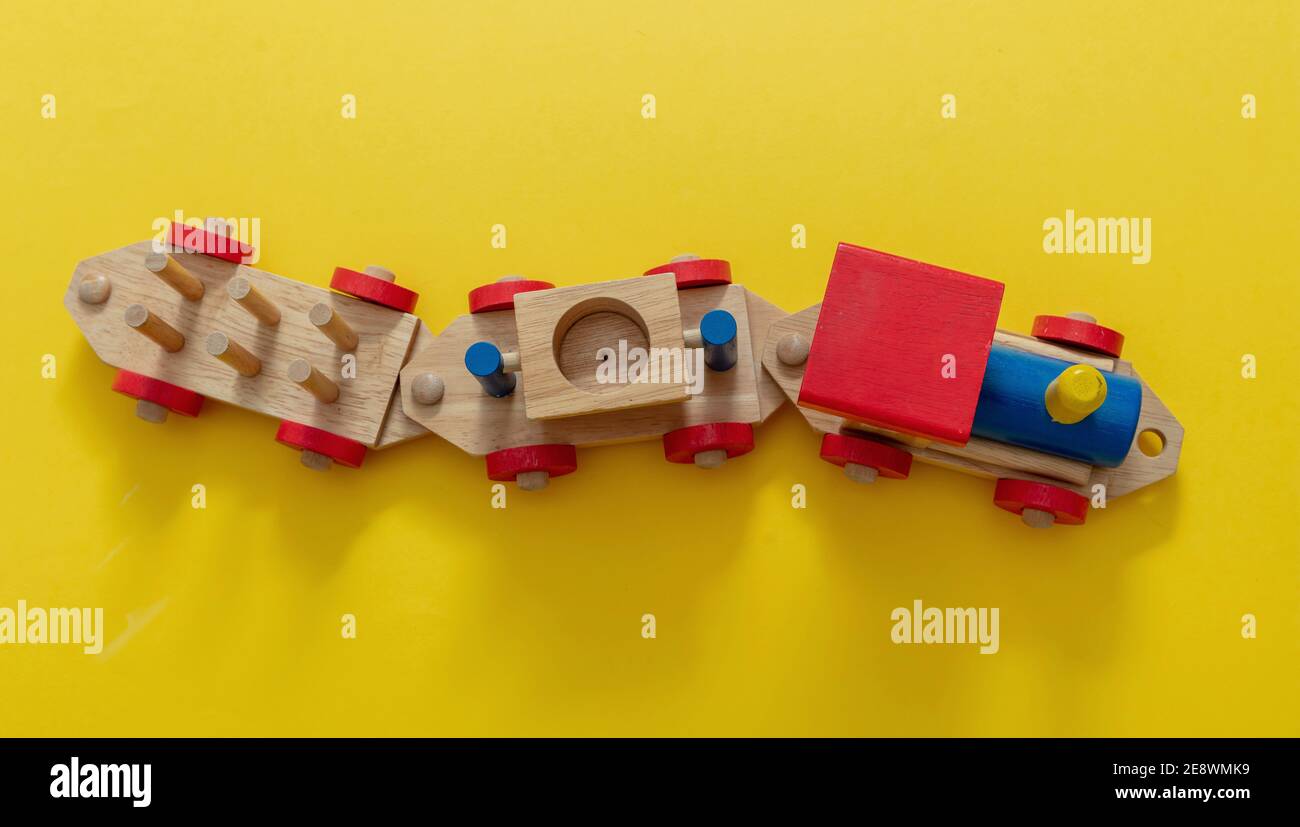 Train children toy, preschool kids game. Locomotive and carriages, wooden colorful blocks construction on yellow color background, top view Stock Photo