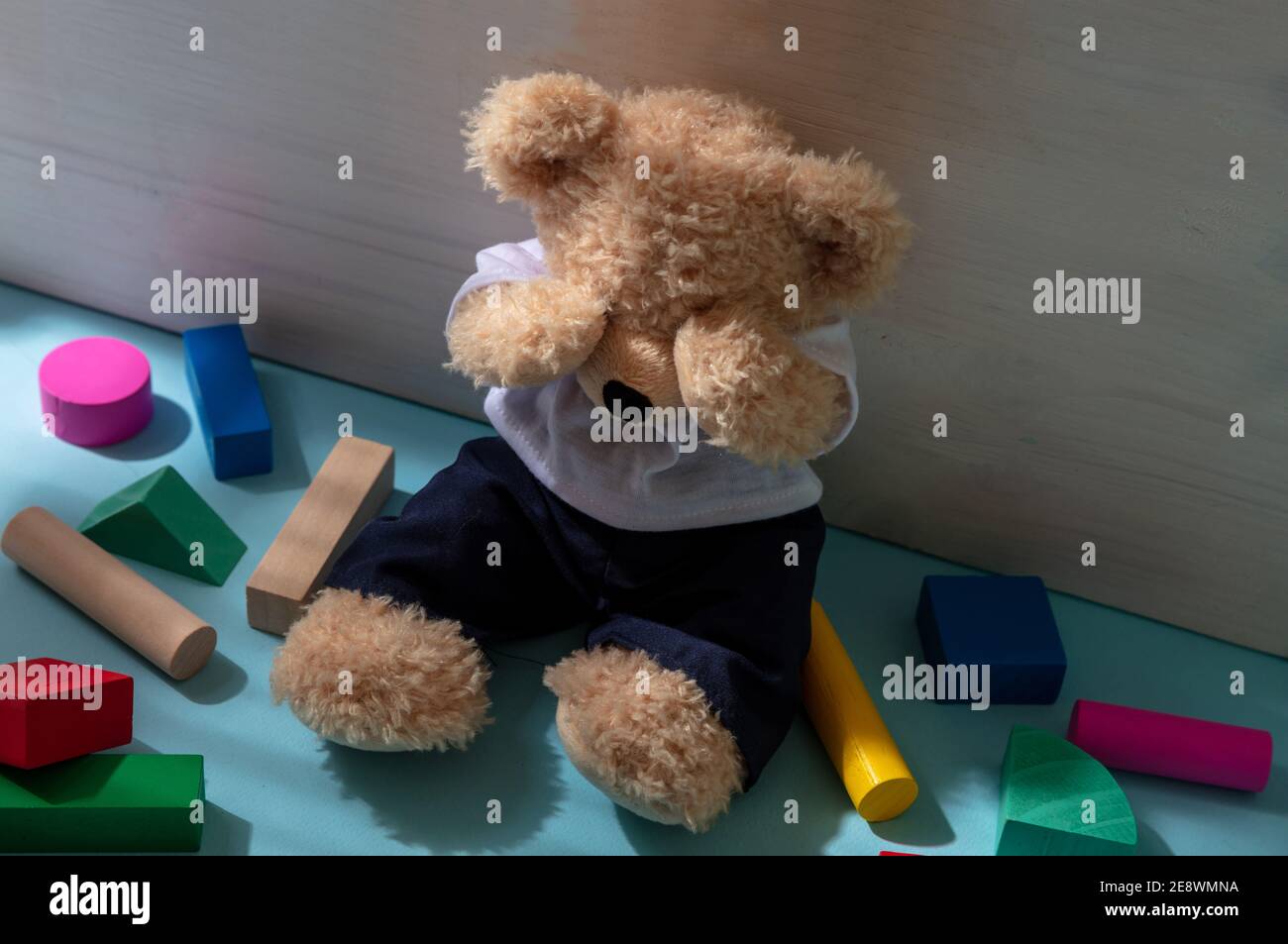 Child abuse concept. Teddy bear covering eyes, sitting on child room floor, colorful wooden blocks around Stock Photo