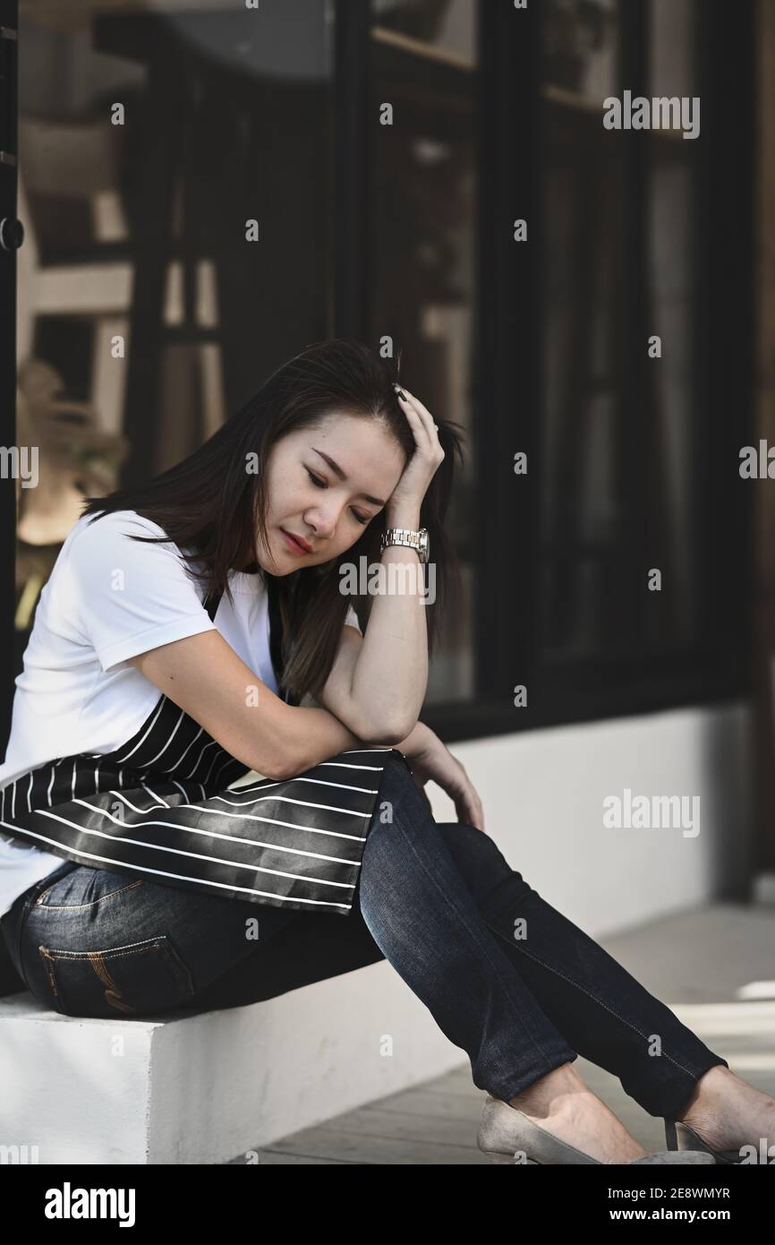 Asian woman coffee shop owner stressed and disappointed from business losses. Stock Photo
