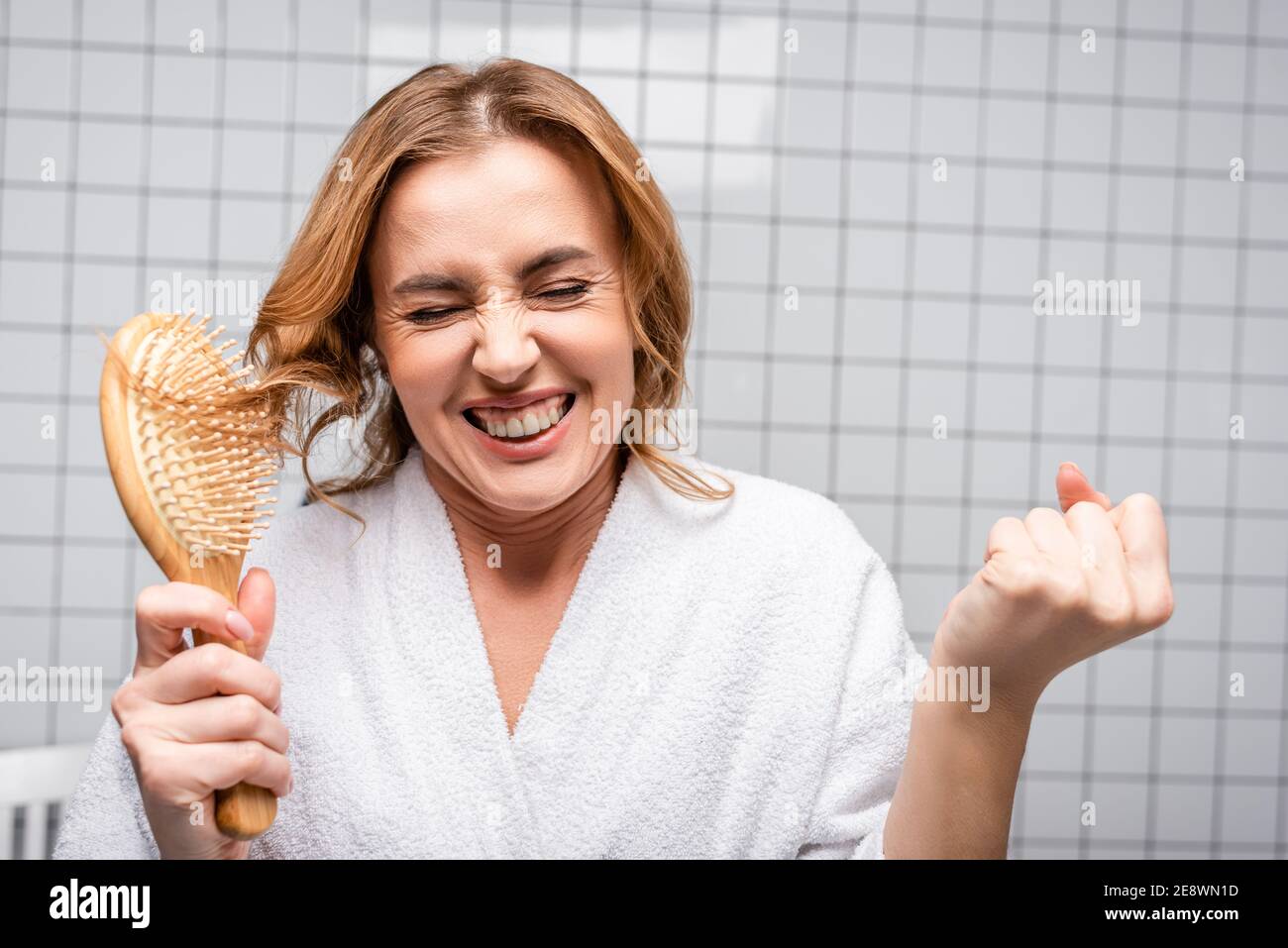 amazed woman in white bathrobe brushing hair in bathroom Stock Photo