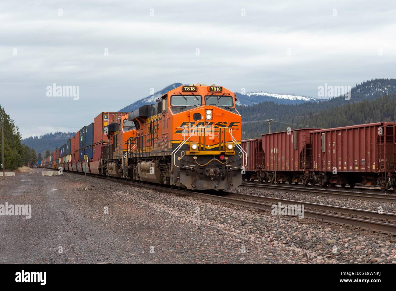 A BNSF train diesel electric locomotive pulling a line of container well cars through the rail yard in Troy, Montana.   Burlington Northern and Santa Stock Photo