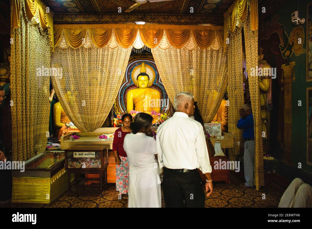 Sri Lanka. Sinhalese people standing in front of a golden buddha Statue in a temple at an altar. Stock Photo