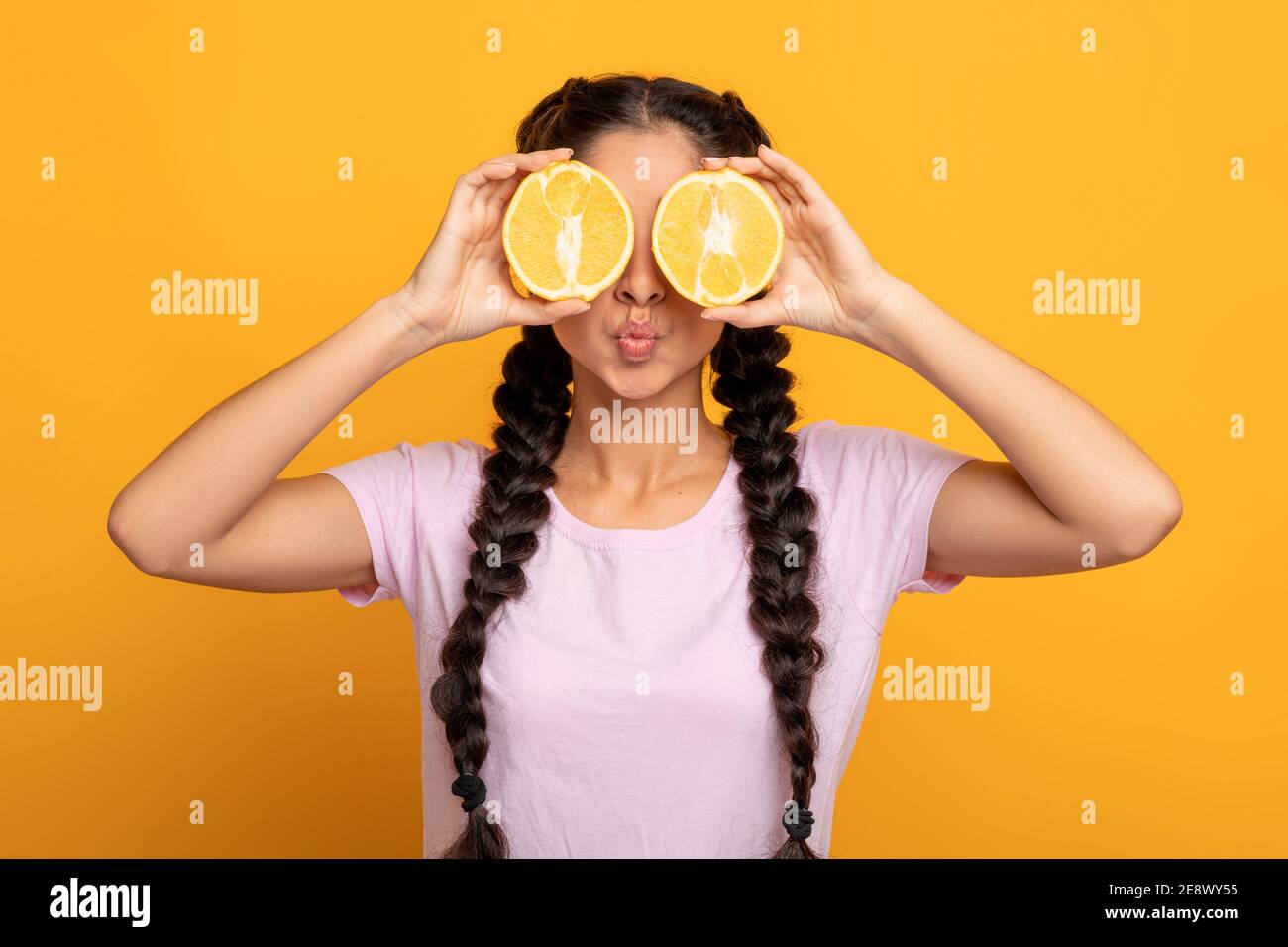 Indian lady covering eyes with halves of citrus orange fruit Stock Photo