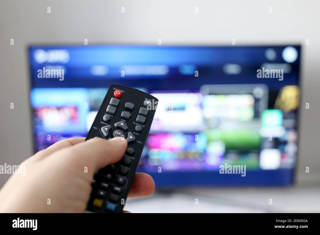 Male hand with remote controller on smart TV screen background. Person choosing streaming services, watching movies Stock Photo