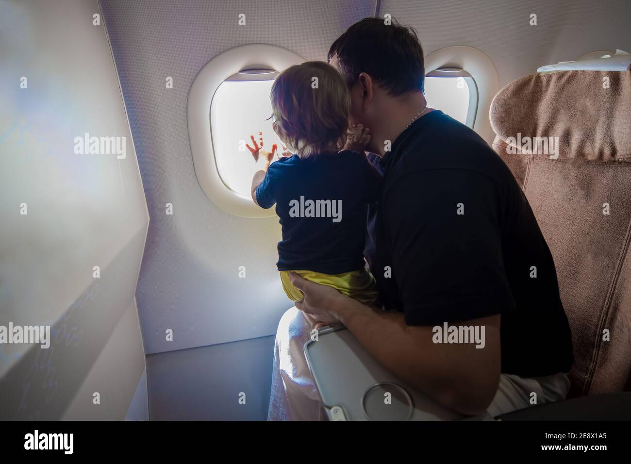 father and cute Toddler sitting on an airplane and looking at the sky through the porthole. first flight concept, traveling with children Stock Photo