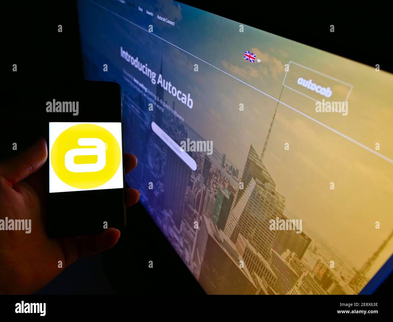 Person holding cellphone with logo of British taxi software development company Autocab Ltd on display in front of web page. Focus on phone screen. Stock Photo