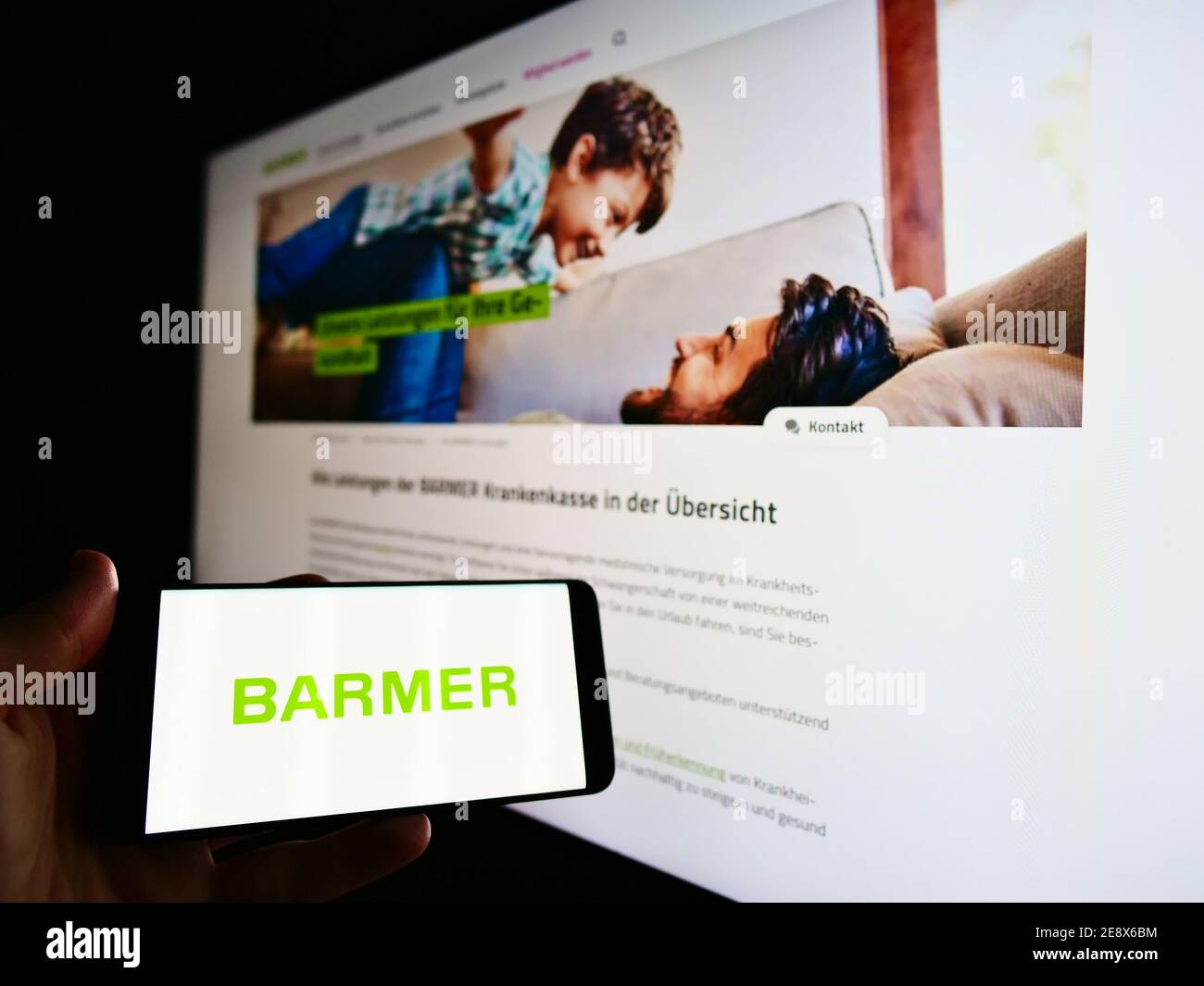 Person holding mobile phone with logo of German health insurance Barmer Ersatzkasse on display in front of company website. Focus on phone screen. Stock Photo