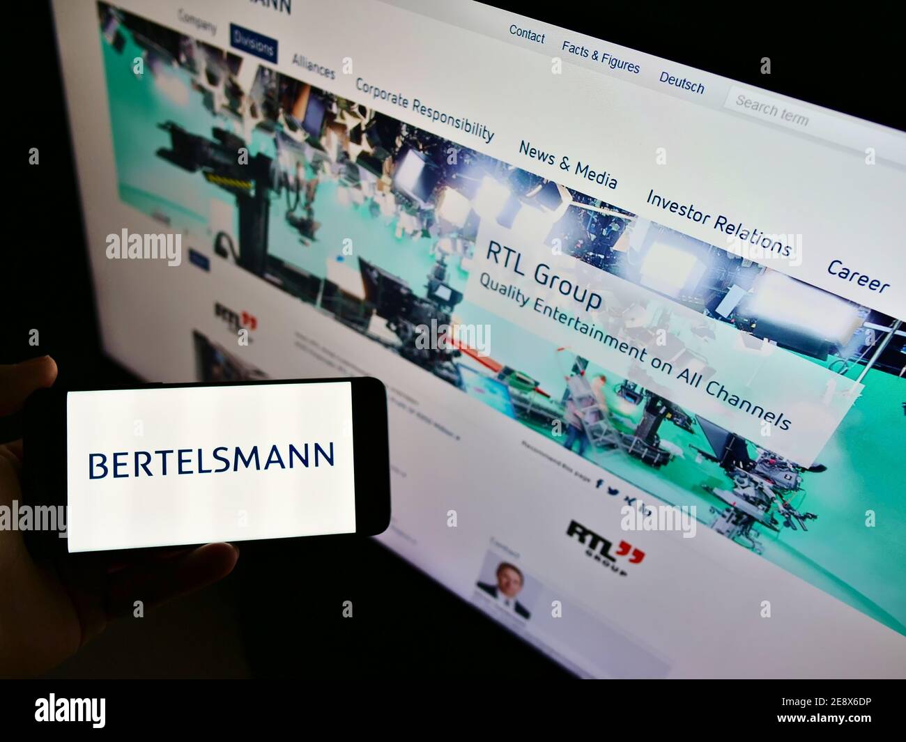 High angle view of person holding smartphone with logo of German mass media conglomerate Bertelsmann on display. Focus on mobile phone screen. Stock Photo