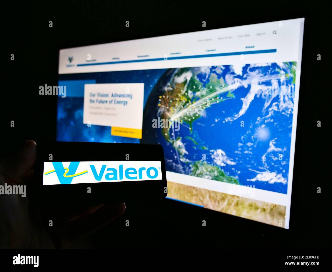 Person holding mobile phone with logo of US petrochemical company Valero Energy Corporation on screen in front of web page. Focus on phone display. Stock Photo