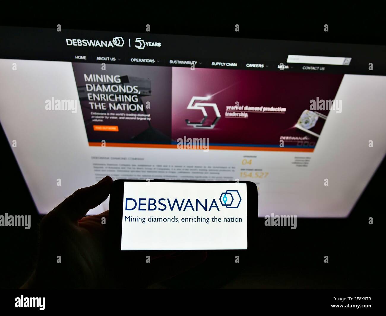 Person holding smartphone with logo of mining company Debswana Diamond Company Limited on display in front of website. Focus on mobile phone screen. Stock Photo