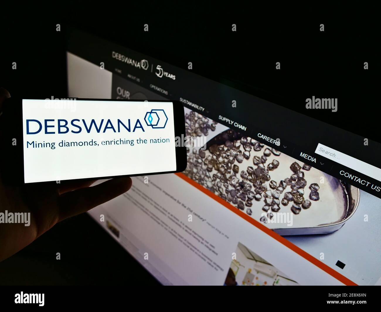 Person holding cellphone with logo of mining company Debswana Diamond Company Limited on display in front of business website. Focus on phone screen. Stock Photo