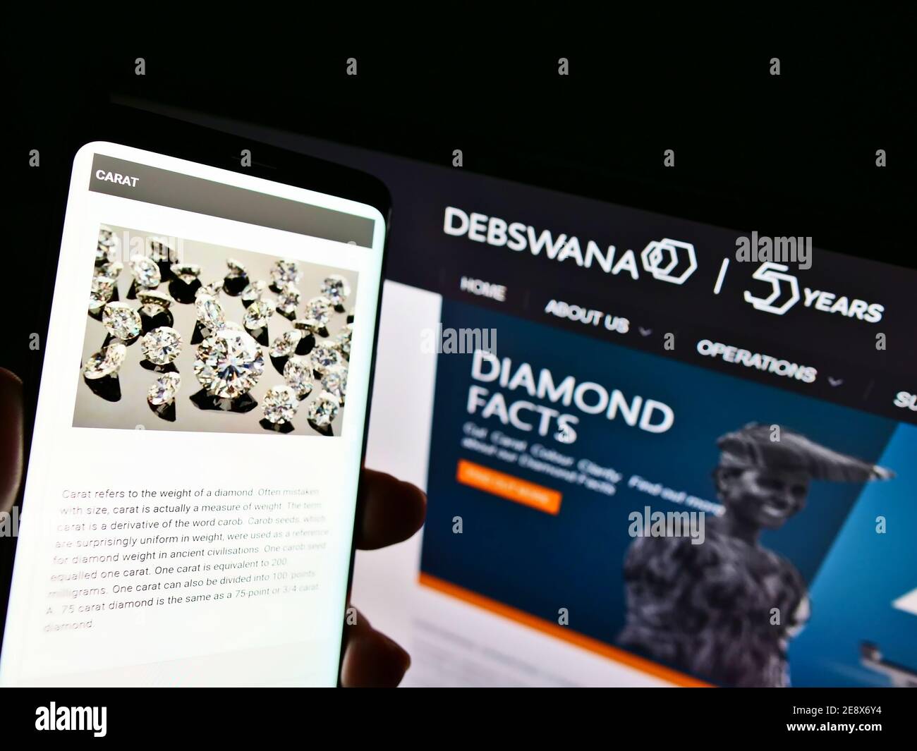 Person holding smartphone with website of mining company Debswana Diamond Company Limited in front of logo. Focus on top center of phone screen. Stock Photo
