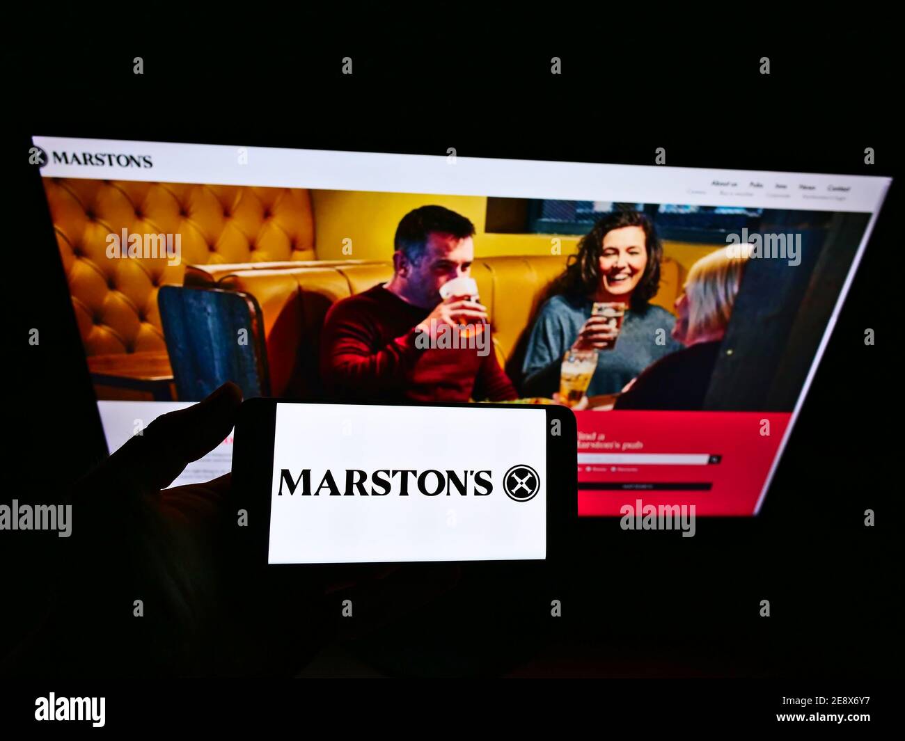 Person holding smartphone with logo of British brewery, hotel and pub operator Marston's plc on display in front of website. Focus on phone screen. Stock Photo