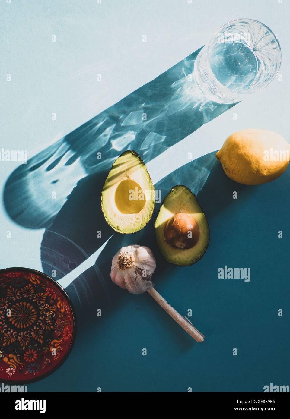 Ingredients for fresh Mexican Guacamole, two Avocado halves, garlic and lime/ lemon isolated on turquoise blue background Stock Photo