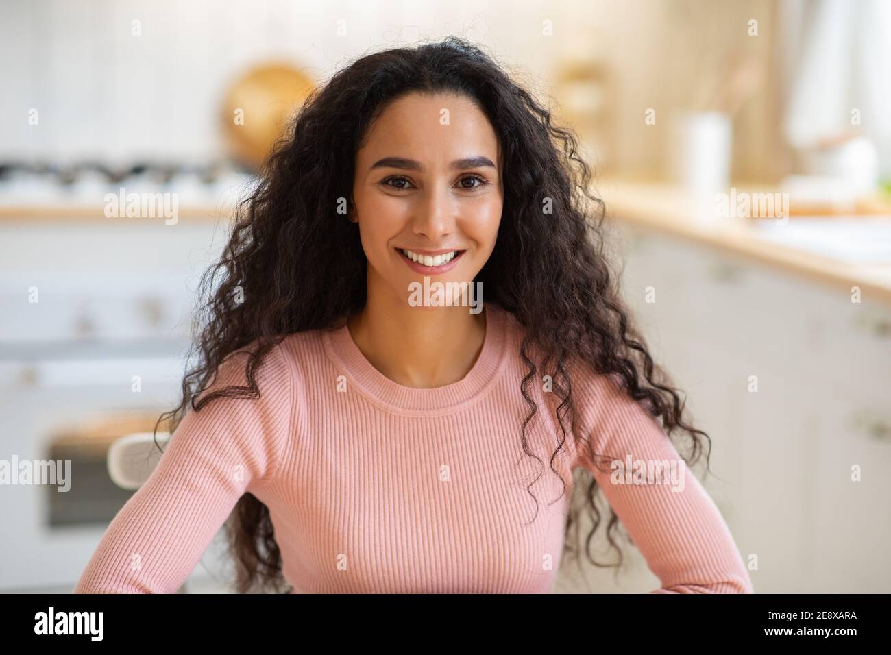 Portraif of happy young brunette woman sitting at table in kitchen Stock Photo