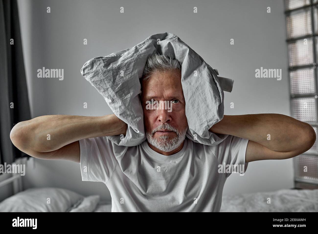 elderly man is tired of hearing voices, schizophrenia, closes ears with blanket, at home alone