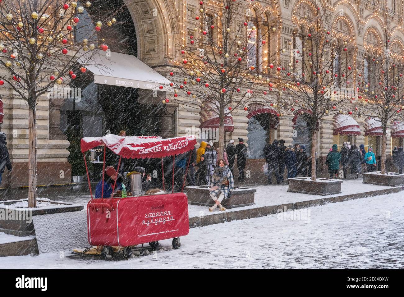 Snowfall in Moscow.Street with Christmas illumination and vintage red street food cart on wheels. Stock Photo