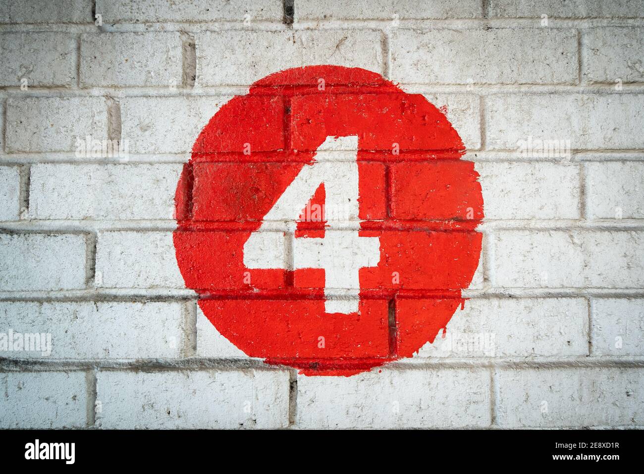 White coloured hand painted level number four in the middle of a red circle painted on an old textured brick wall with runs in the colour Stock Photo