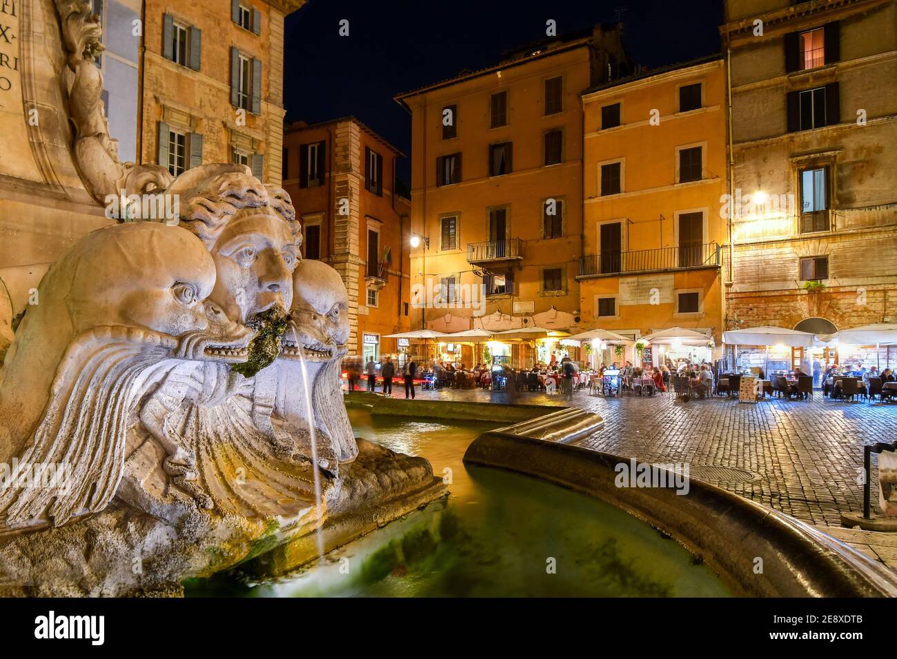 Closeup of the Pantheon Fountain or Fontana del Pantheon in the Piazza della Rotonda at night with sidewalk cafes and shops illuminated in Rome Italy Stock Photo