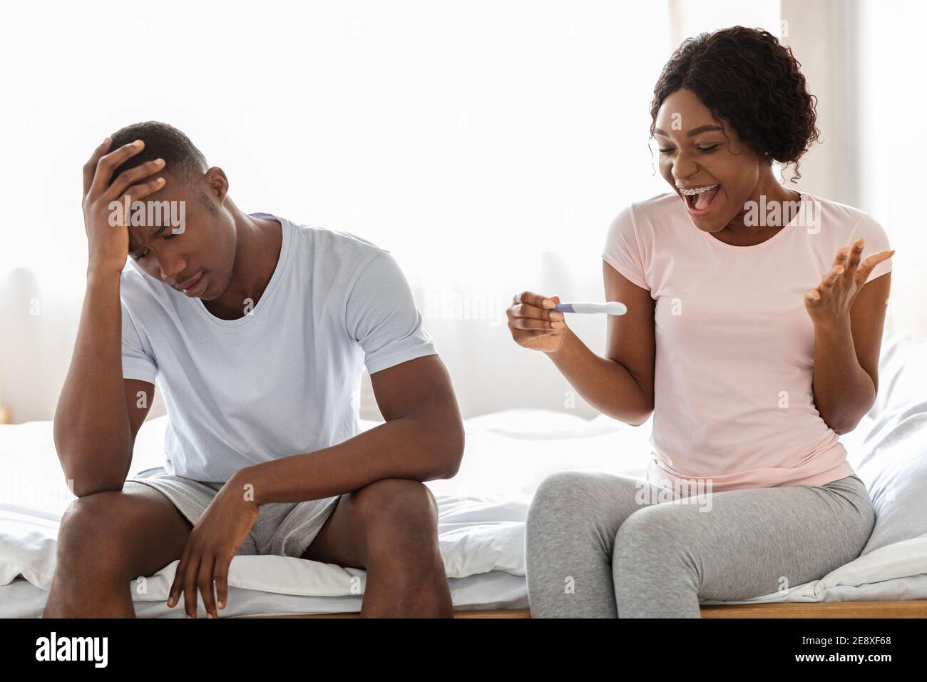 Happy black woman with pregnancy test and her unhappy boyfriend Stock Photo