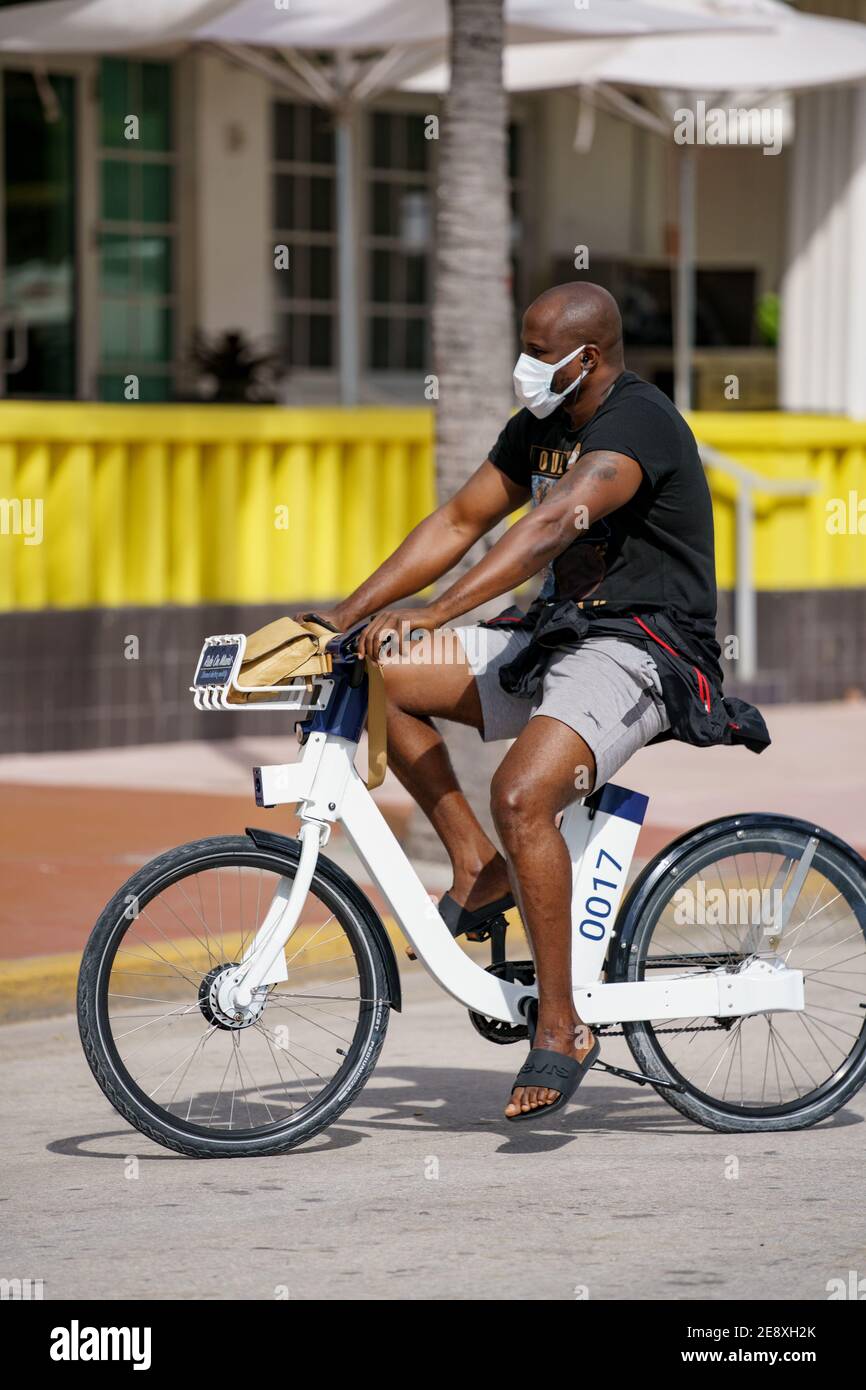 Man wearing a face mask while riding a bike Miami Beach street ...