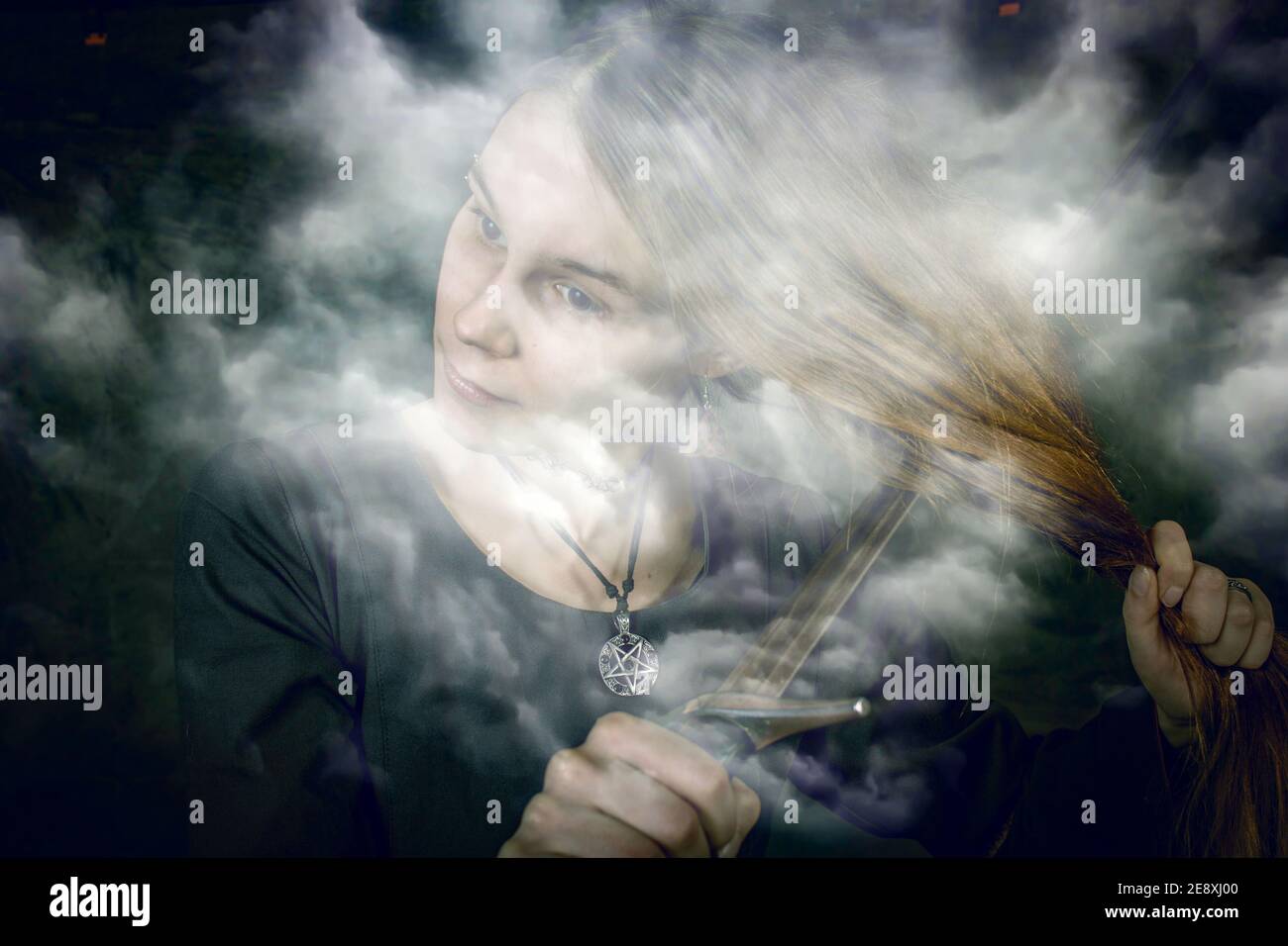 portrait of young long haired woman wearing a medieval costume. standing pose with a sword at her hair at dark studio background Stock Photo