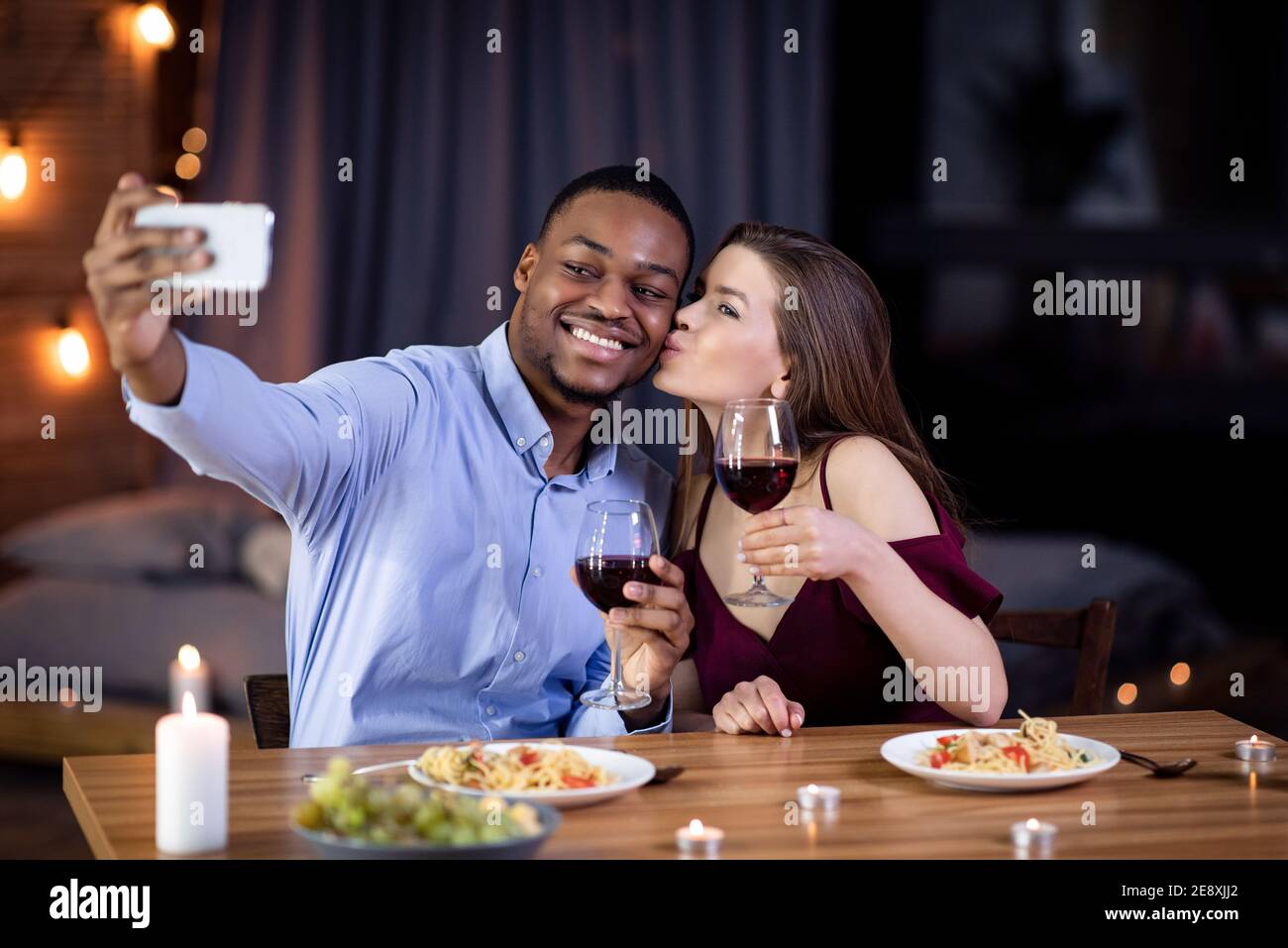 Multiracial couple in love taking selfie while having romantic dinner at restaurant Stock Photo