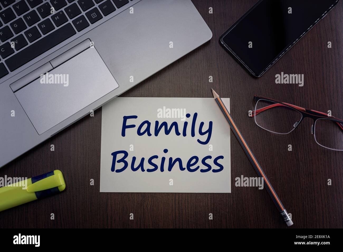 Top view of laptop, phone, glasses and pencil with card with inscription family business. Stock Photo