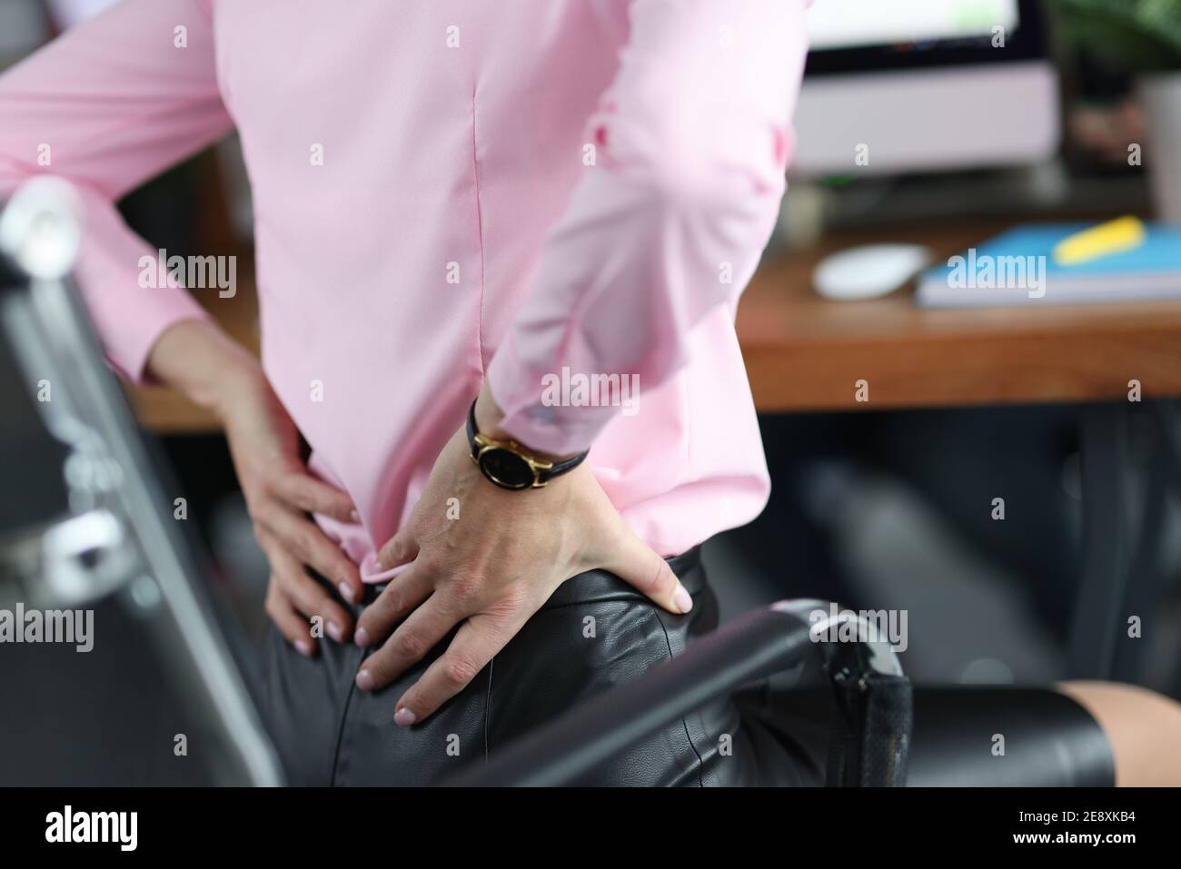 Woman siting on chair in office and holding her lower back closeup ...