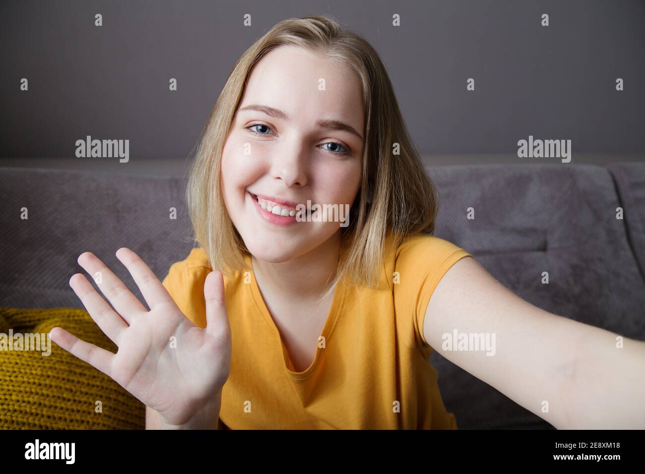 Happy woman portrait wave by hand greeting web camera view. Young beautiful woman talking hi by video call using laptop while sitting on sofa in Stock Photo