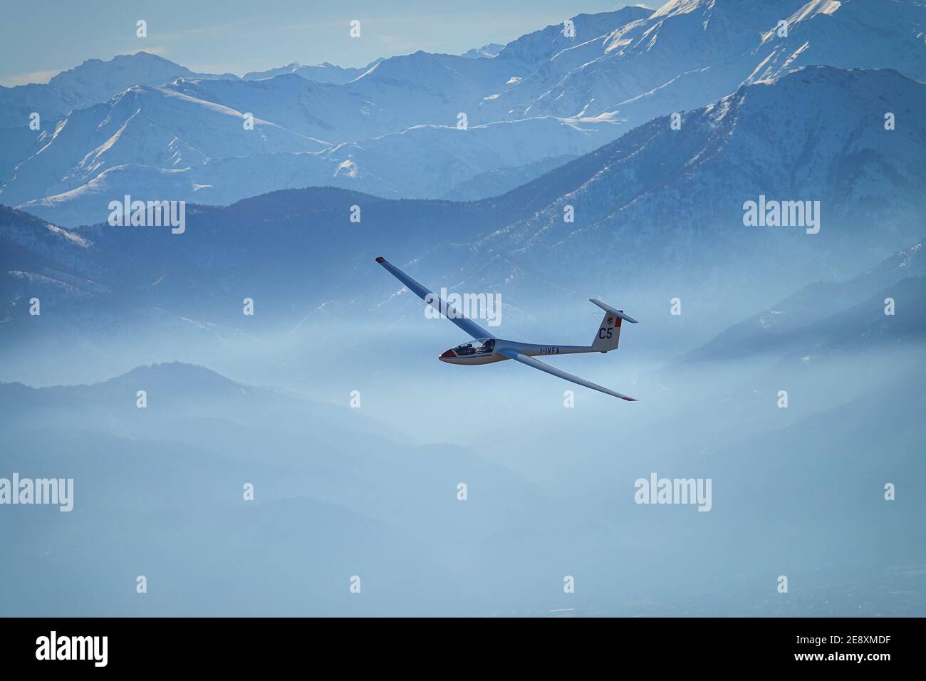 Glider in flight between snowy mountains seen from above. Susa, Italy - January 2021 Stock Photo