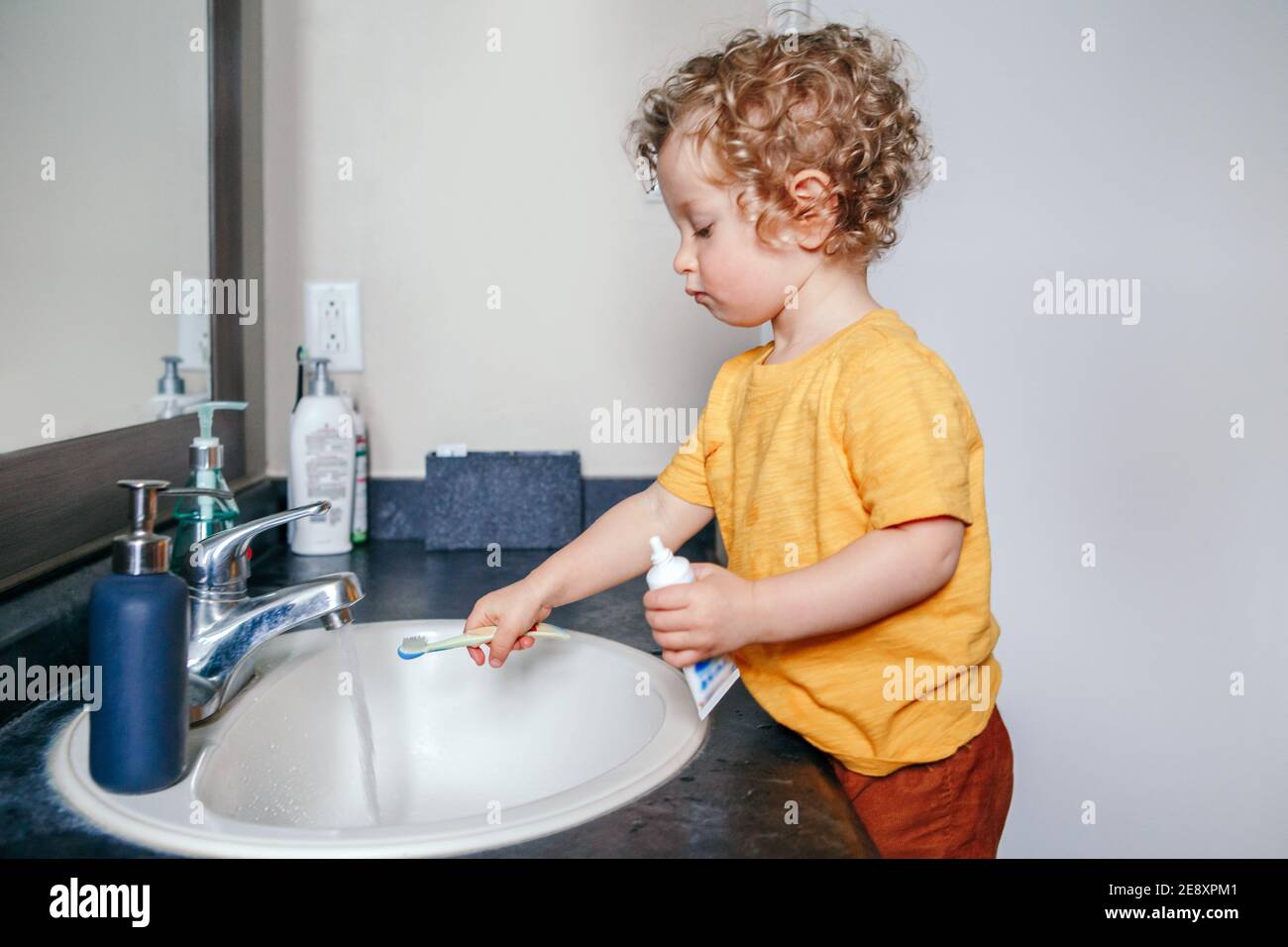 Little Caucasian boy toddler brushing teeth in bathroom at home. Health hygiene and morning routine for children. Cute funny child kid washing in toil Stock Photo