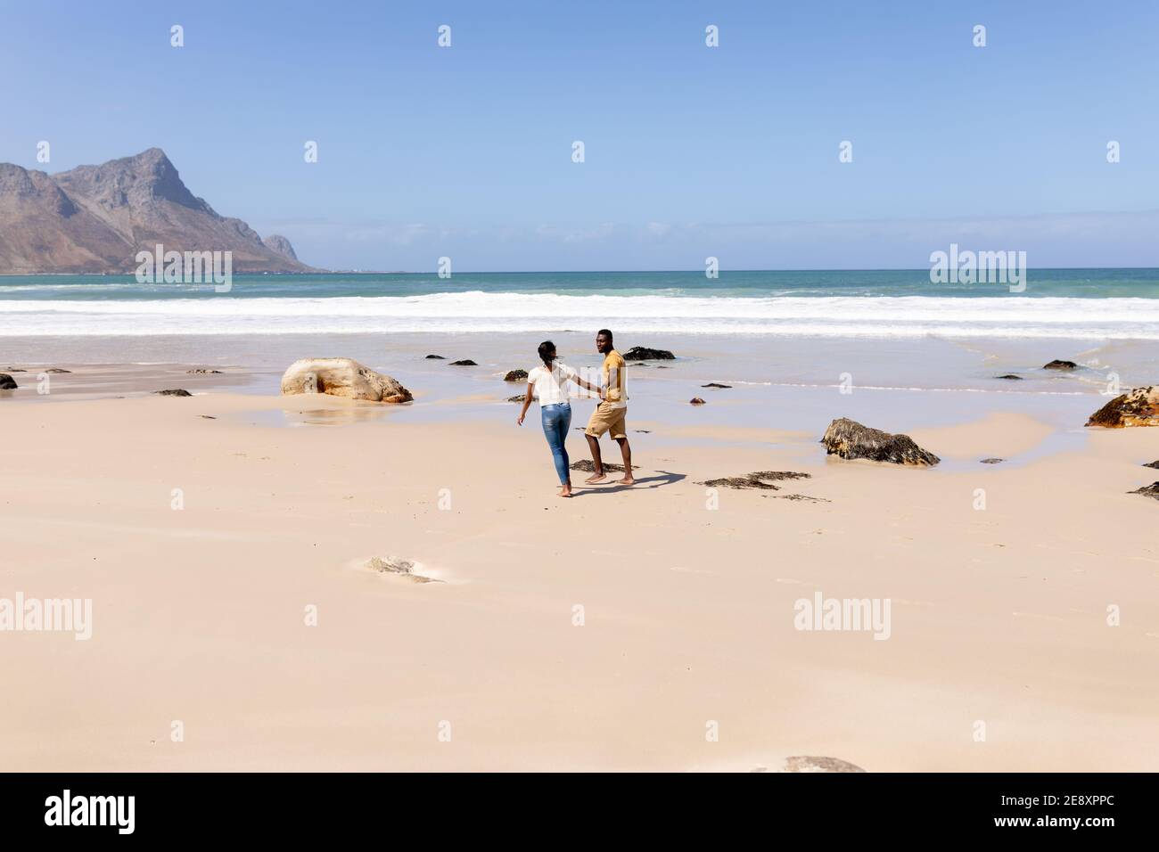African american couple walking holding hands on a beach by the sea ...