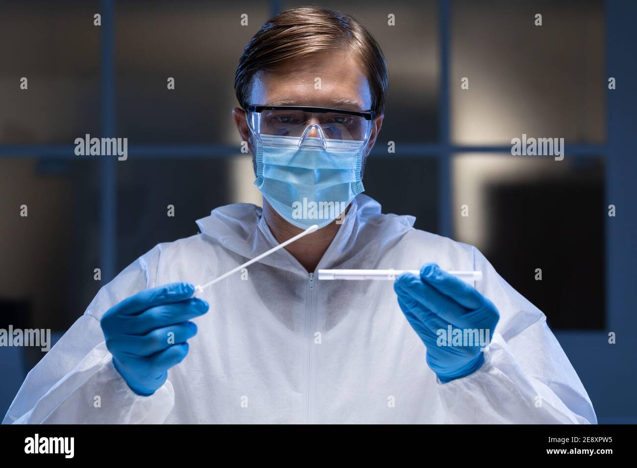 Caucasian male medical worker wearing protective clothing and face mask inspecting swab in lab Stock Photo