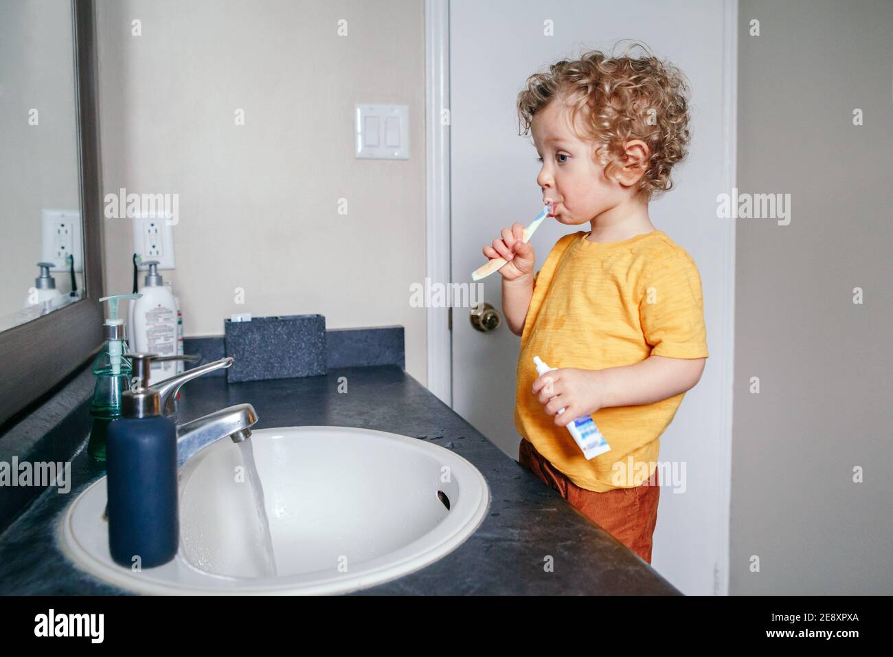 Little Caucasian boy toddler brushing teeth in bathroom at home. Health hygiene and morning routine for children. Cute funny child washing in toilet. Stock Photo