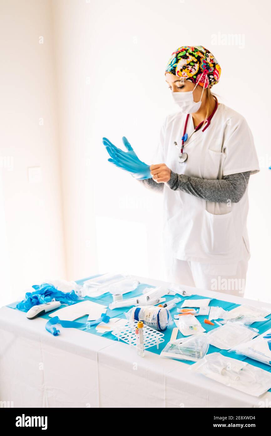Young nurse girl puts on her gloves to attend to patients in front of a table with medical supplies Stock Photo