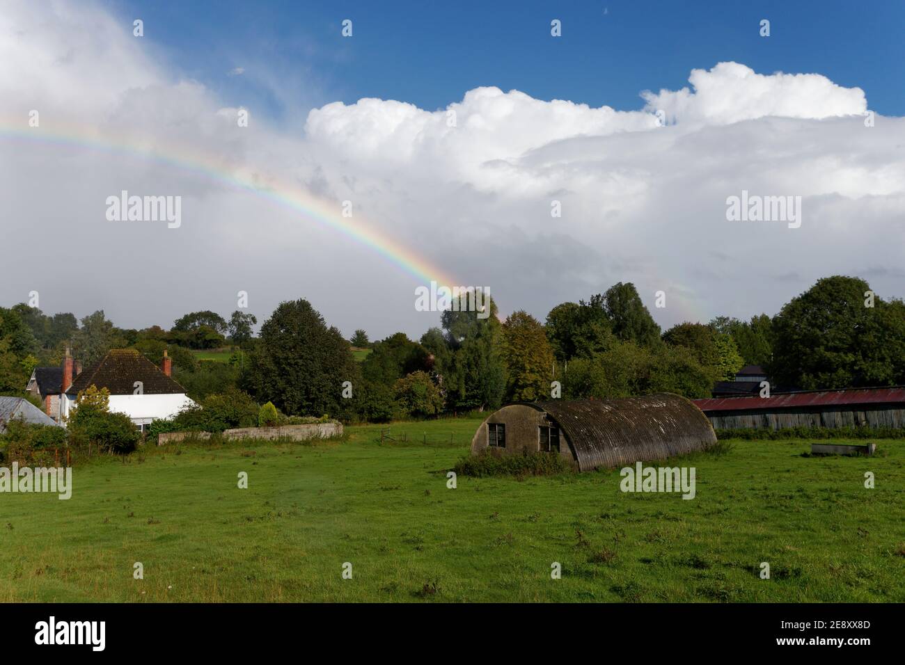 Distant rainbow over a farmers field and white cottage in Wiltshire Stock Photo