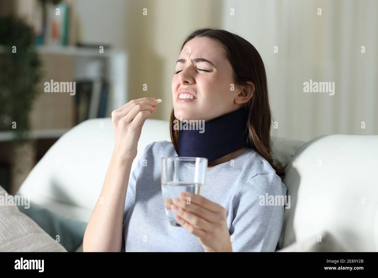 Disabled woman wearing neck brace suffering ache taking pill at home Stock Photo
