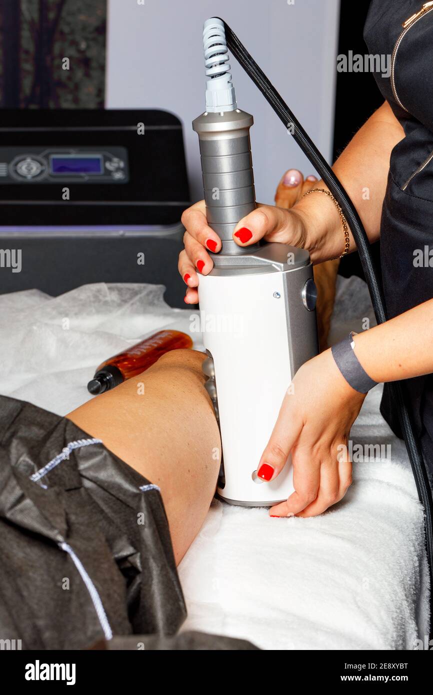 A professional beautician performs an electromagnetic massage of the muscles in the leg using a high-intensity trainer. Stock Photo
