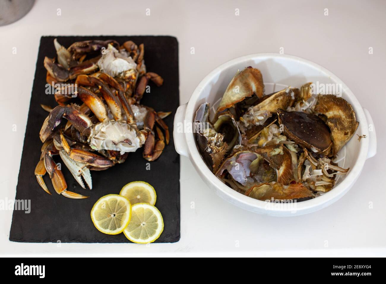 Dungeness crab legs are cleaned and prepared to be cooked for dinner. Crab guts and shells are discarded in a bowl beside them. Stock Photo