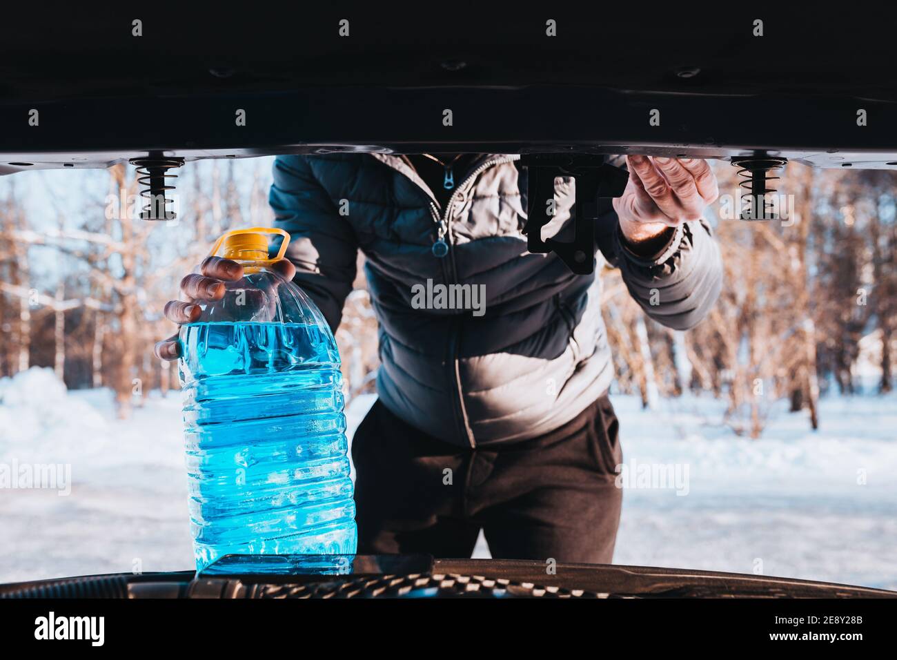 A man opened the hood and pours an antifreeze washer fluid into the