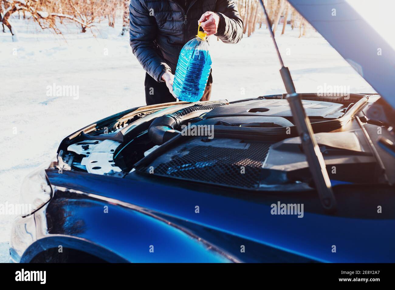 A man opened the hood and pours an anti-freeze washer fluid into the tank - a windshield wiper in winter Stock Photo