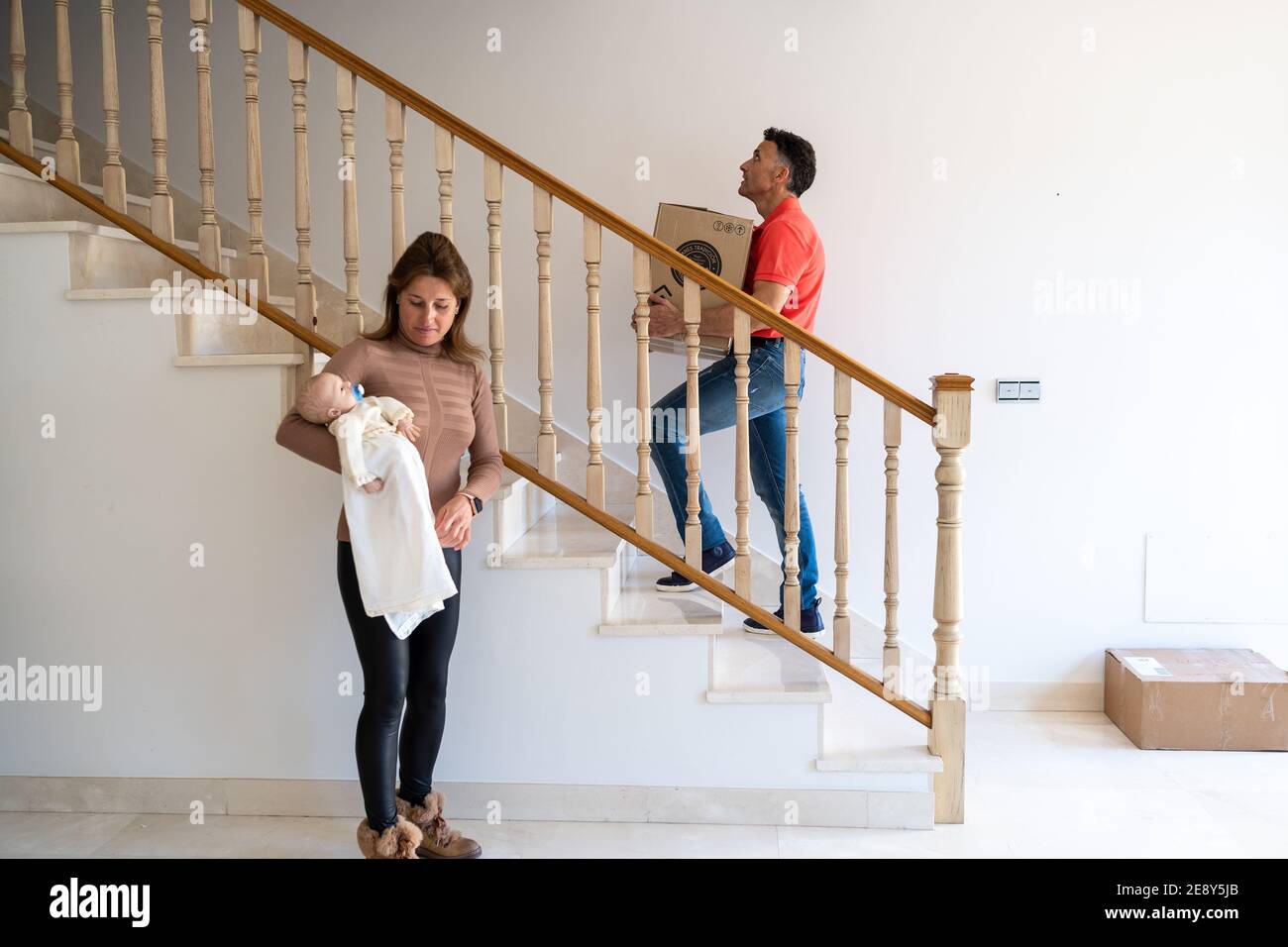Mom carrying a baby while dad moving boxes in the new house Stock Photo ...
