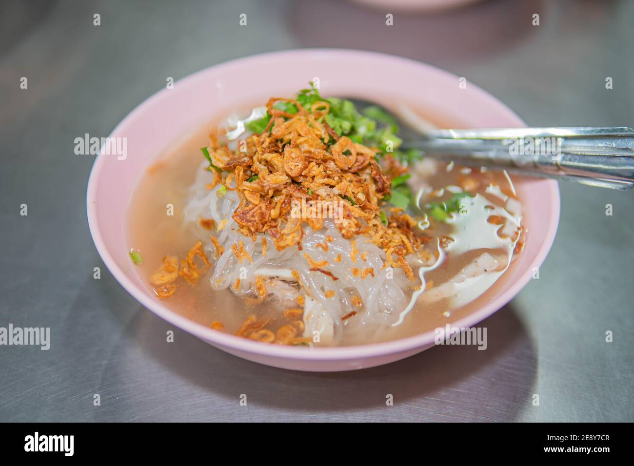 Vietnamese Rice Noodles Soup with pork spare ribs holding in fork and Vietnamese style sausage, deep fried red onion and parsley on wooden table backg Stock Photo