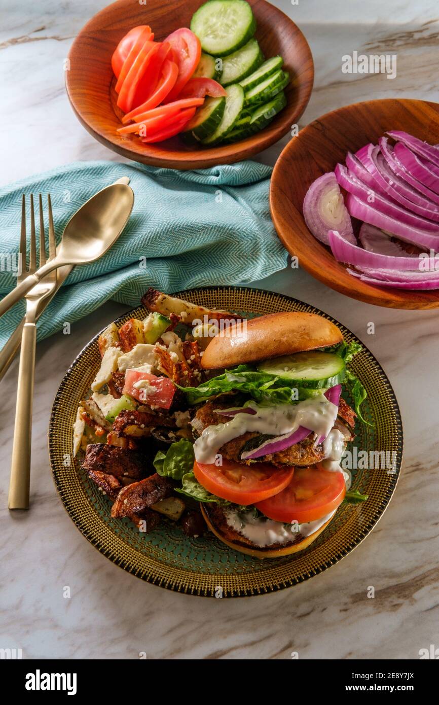 Greek stuffed turkey burger topped with cucumber slices and tzatziki yogurt sauce served with Mediterranean street cart fried potatoes with feta chees Stock Photo