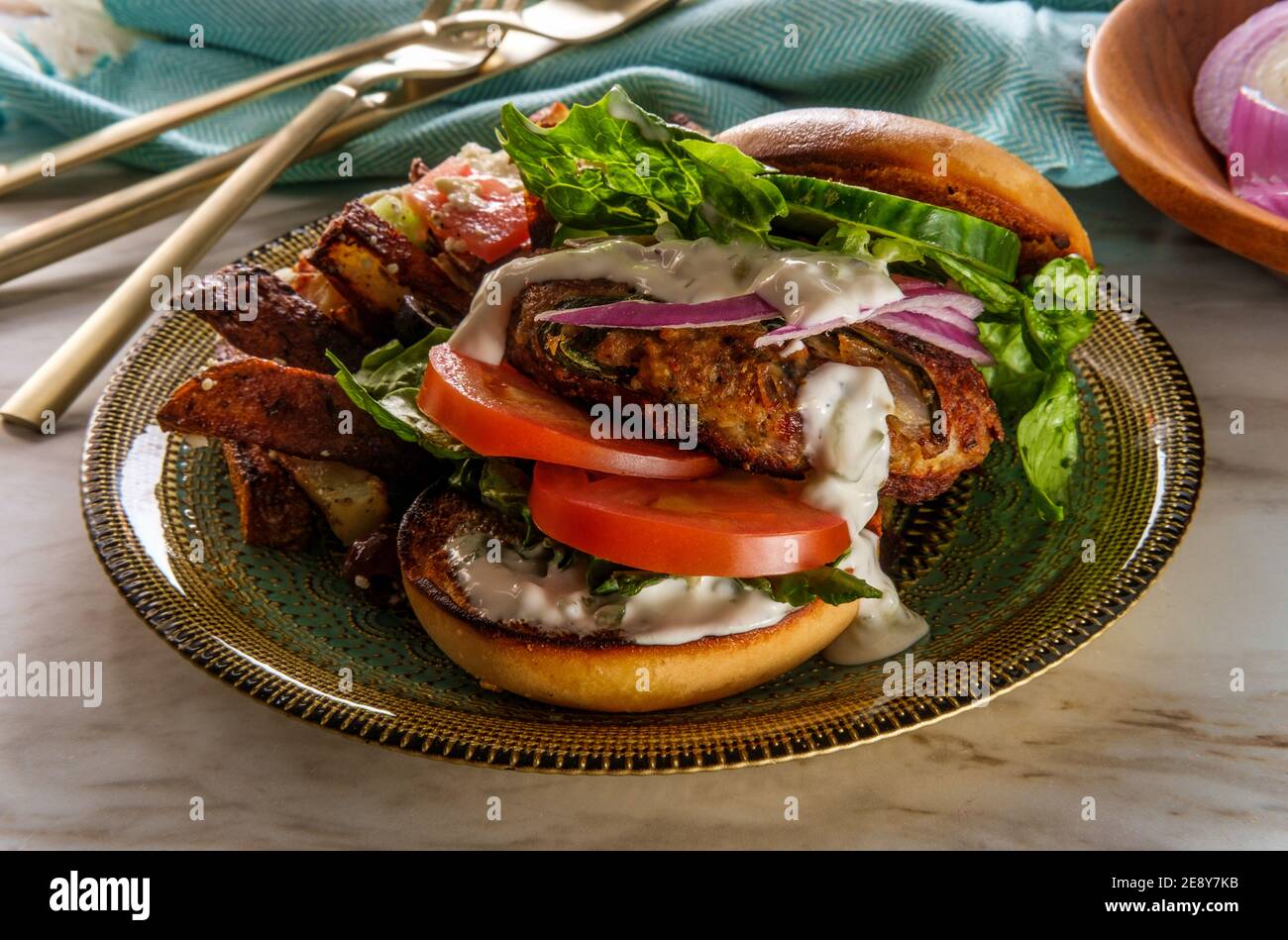 Greek stuffed turkey burger topped with cucumber slices and tzatziki yogurt sauce served with Mediterranean street cart fried potatoes with feta chees Stock Photo