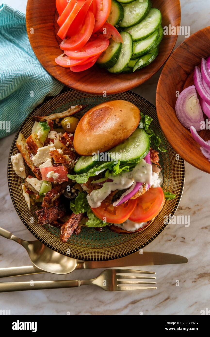 Greek stuffed turkey burger topped with cucumber slices and tzatziki yogurt sauce served with Mediterranean street cart fried potatoes with feta chees Stock Photo