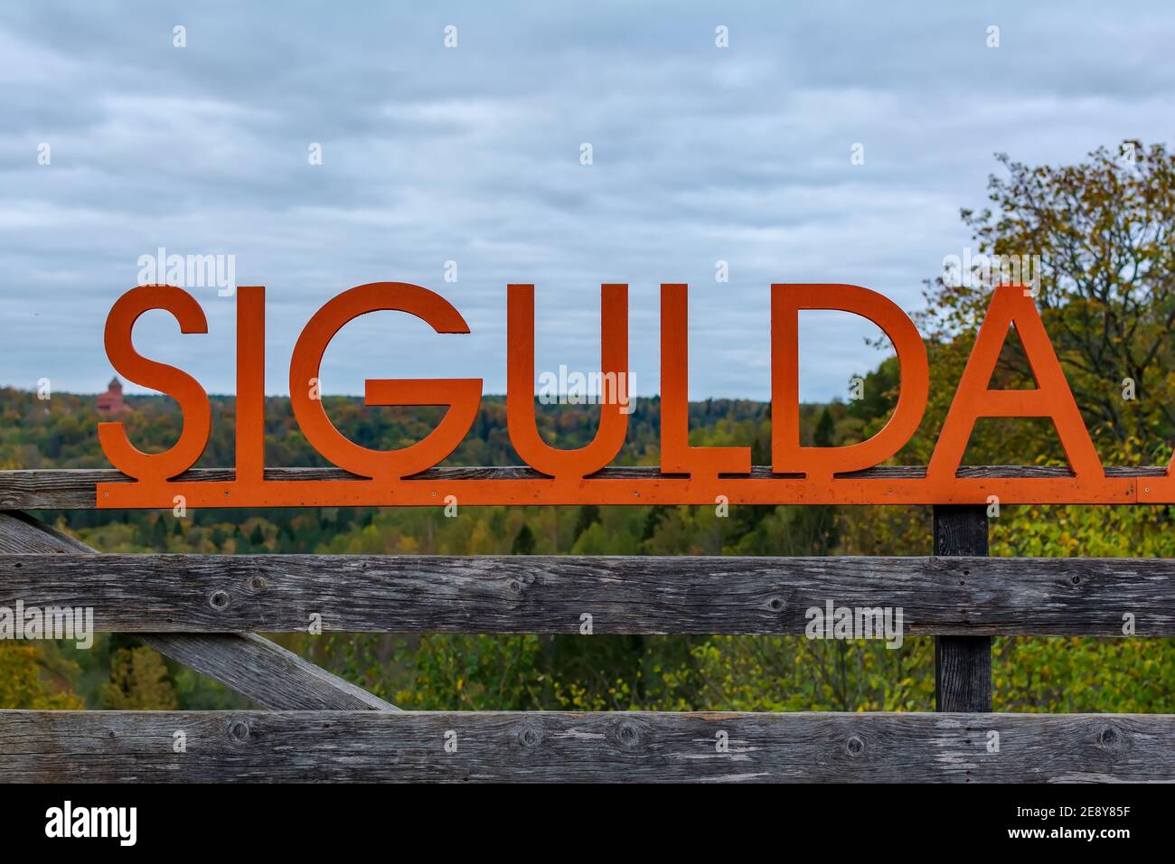 Big orange inscription Sigulda on wooden balustrade of viewpoint in Sigulda Medieval Castle territory, with green forests and Turaida castle silhouett Stock Photo