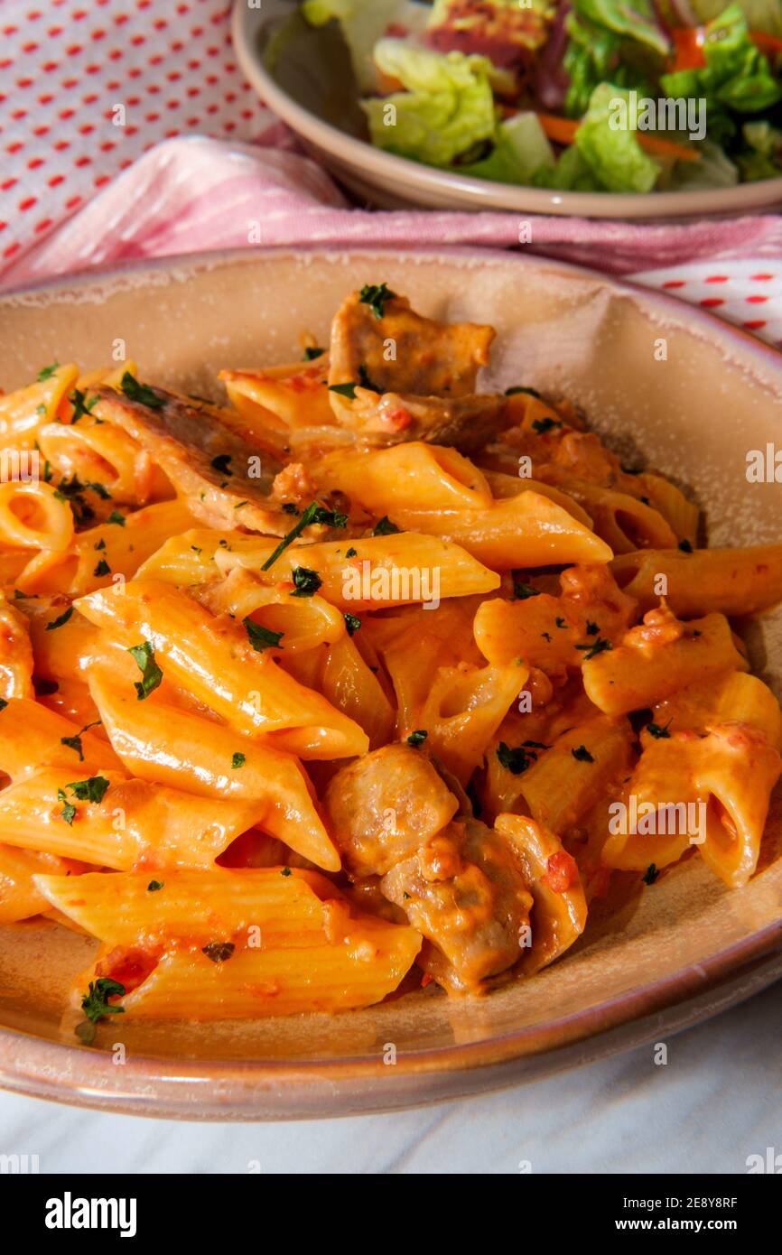 Italian penne alla vodka pink cream sauce with sliced spicy sausage and side salad Stock Photo
