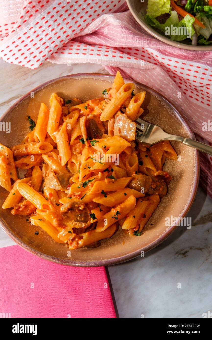 Italian penne alla vodka pink cream sauce with sliced spicy sausage and side salad Stock Photo